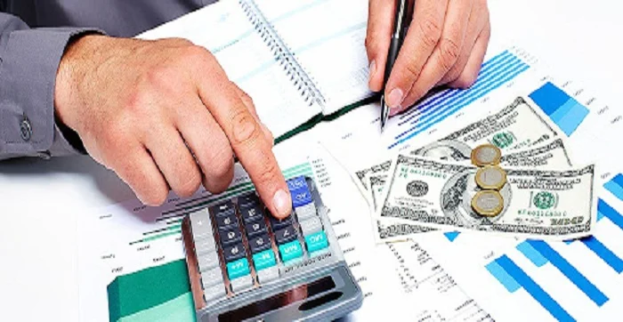 A two hand of man one hand finger in place in calculator and second hand a pen write some in notebook front of up in desk